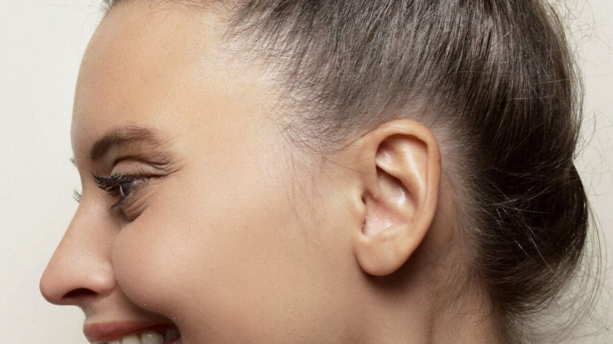 Side profile of a smiling woman with her hair in a bun, ear fully visible