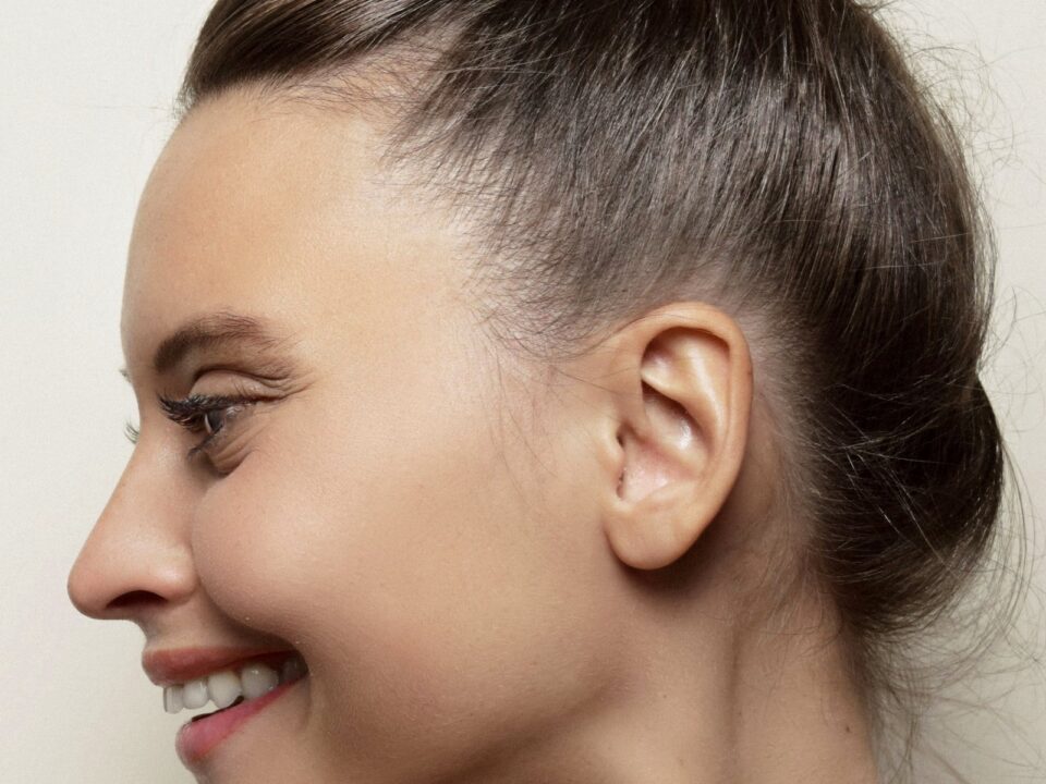 Side profile of a smiling woman with her hair in a bun, ear fully visible